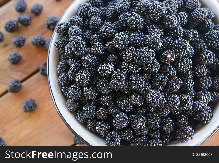 Many blackberries in a metal bowl on wooden background