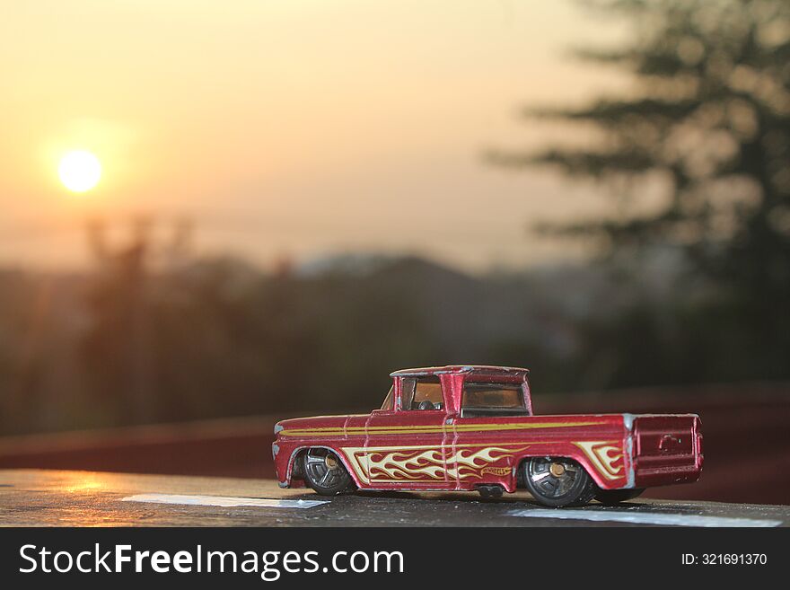 A toy car placed on a wooden block painted to resemble a highway with a morning scene in the background.