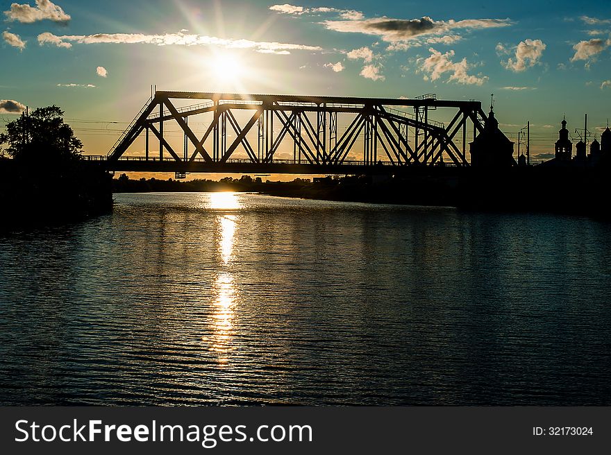 The railway bridge through the river at sunset