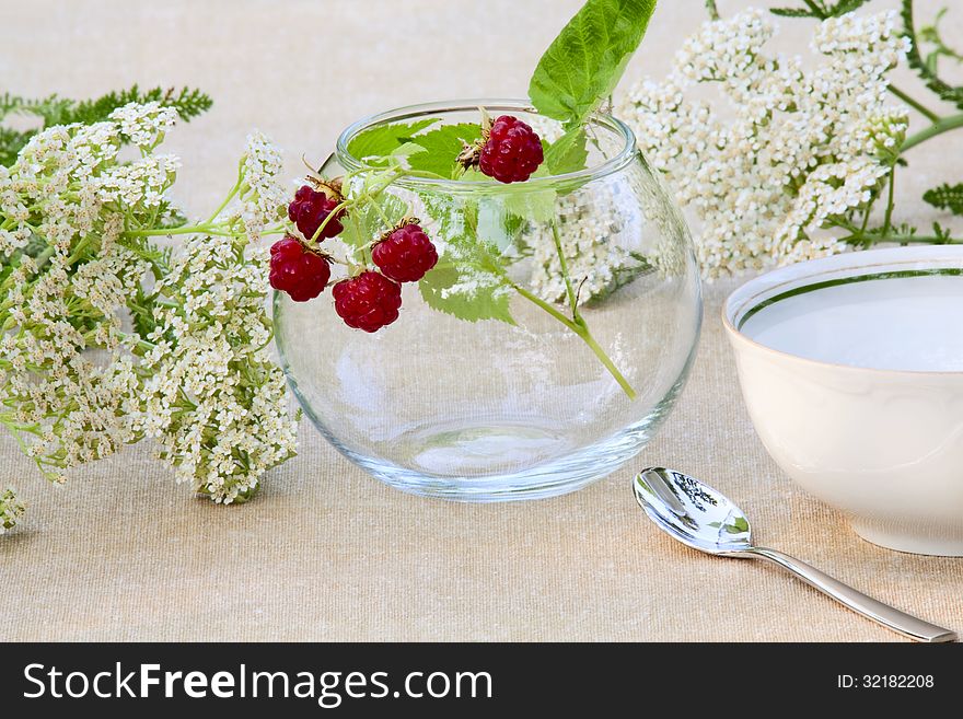 Bunch of raspberries in a glass bowl, wild flowers and tea cup
