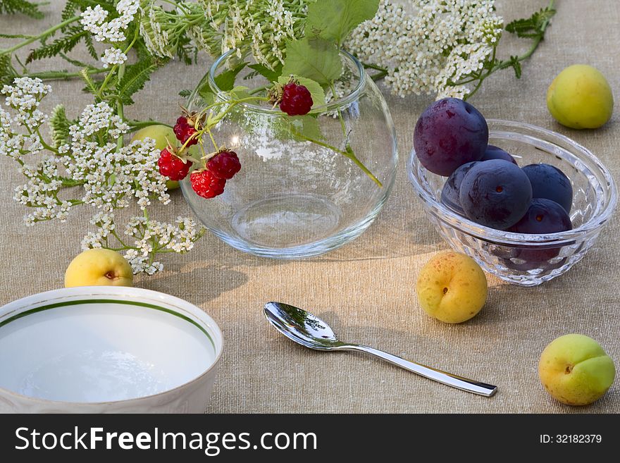 Bunch of raspberries in a glass bowl, plums, apricots, a cup of tea and wildflowers. Bunch of raspberries in a glass bowl, plums, apricots, a cup of tea and wildflowers