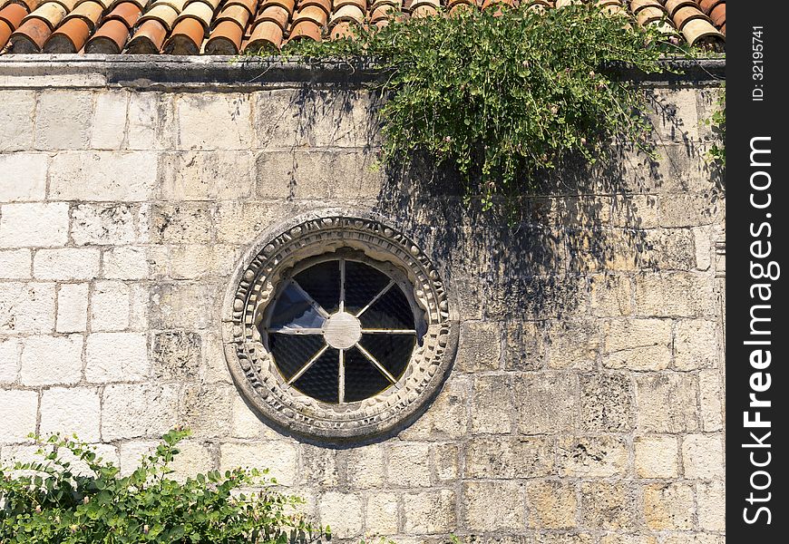 Fragment of ancient building stone wall with round shape window and green plants in Montenegro. Fragment of ancient building stone wall with round shape window and green plants in Montenegro