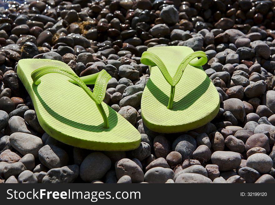 Green women's flip-flops on the pebble beach. Green women's flip-flops on the pebble beach