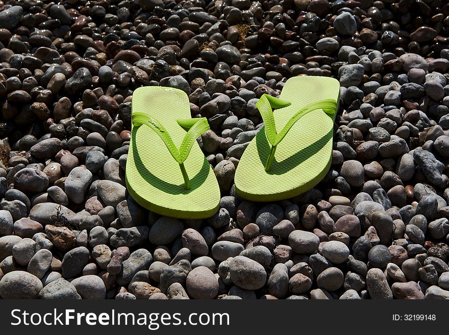 Green women's flip-flops on the pebble beach. Green women's flip-flops on the pebble beach