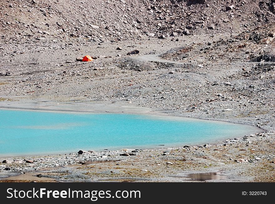 Orange tent next a blue mountain lake, Italy