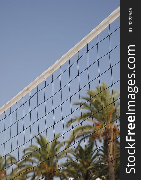 Volleyball net with palm trees against a blue sky