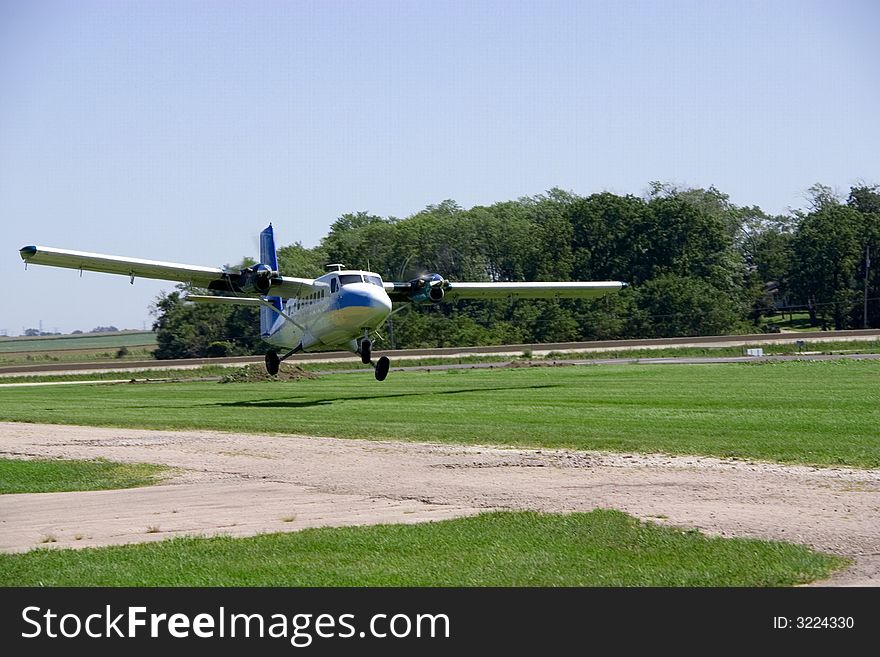 This is a medium sized twin engine propeller airplane landing on a grass landing strip. This is a medium sized twin engine propeller airplane landing on a grass landing strip.