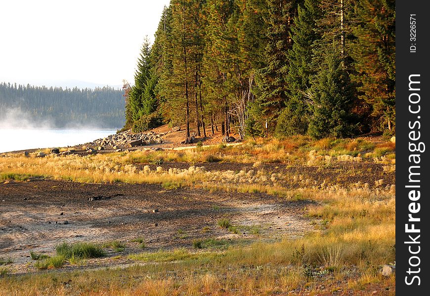 Morning light at Crescent Lake, Oregon. We see the fog lifting from the water of the lake, autumn colors are just beginning to show in the trees and plants around the lake. Morning light at Crescent Lake, Oregon. We see the fog lifting from the water of the lake, autumn colors are just beginning to show in the trees and plants around the lake