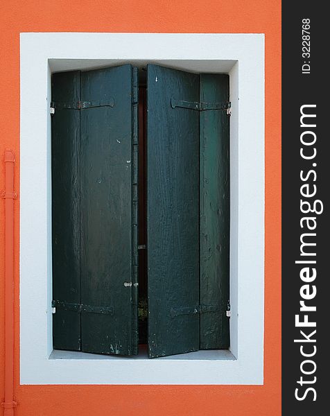 Closed window on a bright orange wall of a house on the island of Burano, outside of Venice Italy. Closed window on a bright orange wall of a house on the island of Burano, outside of Venice Italy.