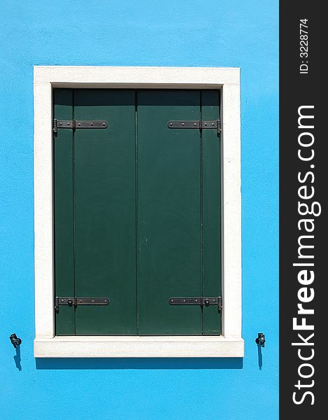 Closed window on a bright blue wall of a house ont he island of Burano, outside of Venice Italy. Closed window on a bright blue wall of a house ont he island of Burano, outside of Venice Italy.