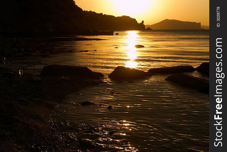 Early morning on the beach . Mountains are visible as silhouettes. 
Water of gold color. Early morning on the beach . Mountains are visible as silhouettes. 
Water of gold color.