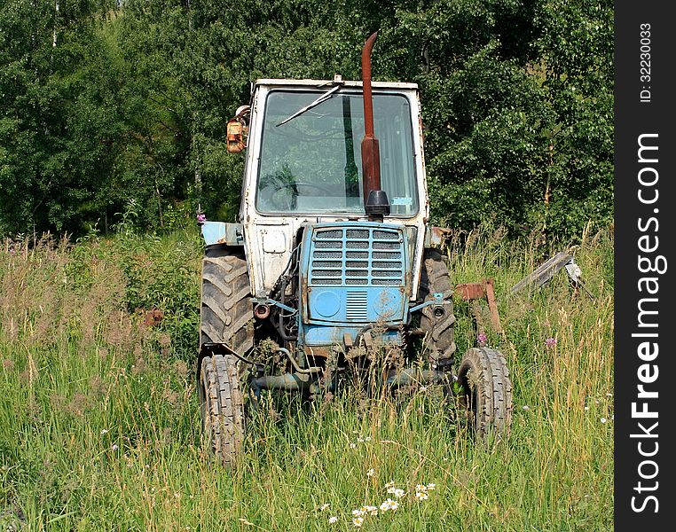 The old tractor in a field on a background of forest. The old tractor in a field on a background of forest