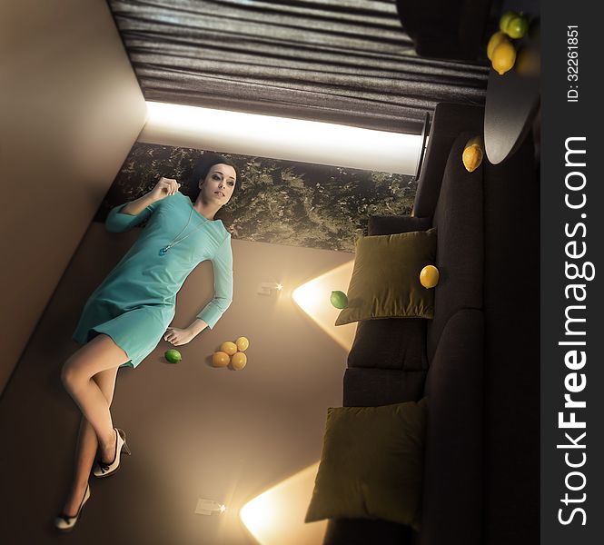 Extraordinary beautiful woman lying and relaxing on the wall in the overturned room with lemons