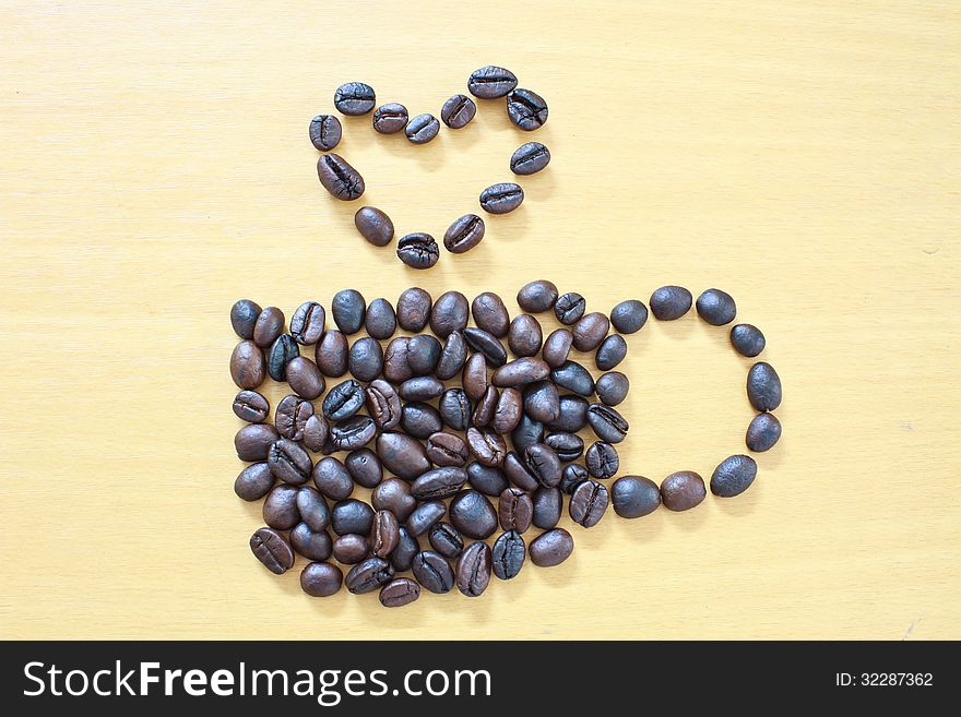 Coffee cup with heart image made up of coffee beans on wood background