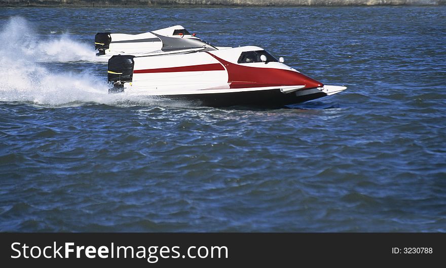 Two white formula one outboards side by side at full speed in competition on blue water of a river.