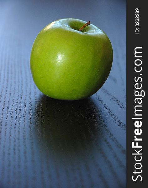 One green apple on dark colored table.