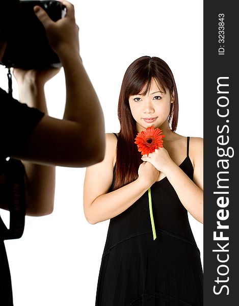 A photographer taking a picture of n attractive young Asian woman in white top holding a red flower on white background. A photographer taking a picture of n attractive young Asian woman in white top holding a red flower on white background
