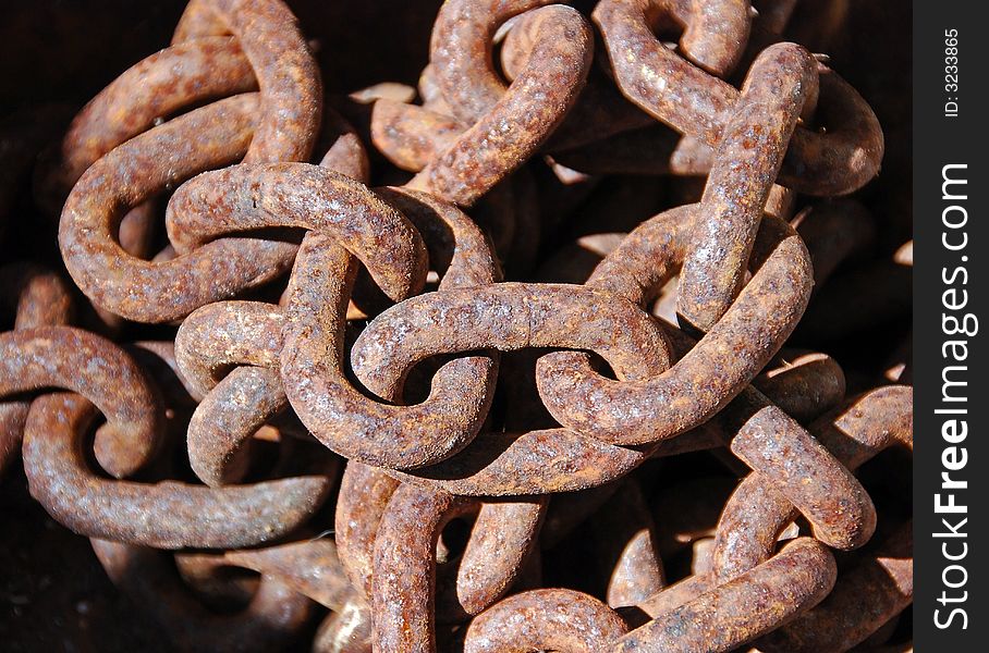 A close-up rusty chain left heaped in a pile in the sun.