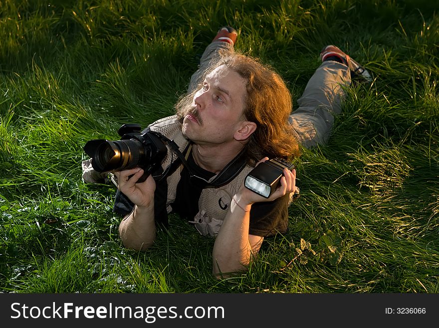 The photographer with the camera lays on a green grass. The photographer with the camera lays on a green grass