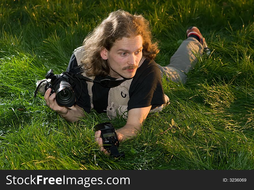 The photographer with the camera lays on a green grass