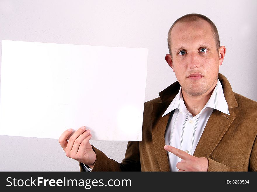 A young businessman is holding a sign and points at it! White sign to write on!. A young businessman is holding a sign and points at it! White sign to write on!