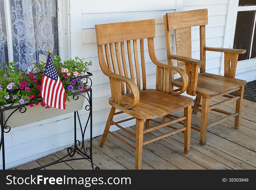 Two wooden chairs on old front porch with flowers and american flag. Two wooden chairs on old front porch with flowers and american flag