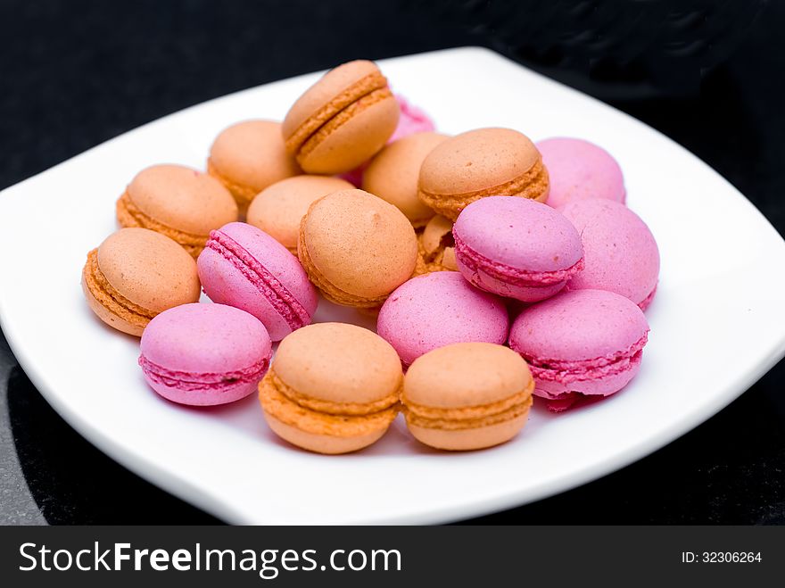 Heap of macaroons in white plate on black background