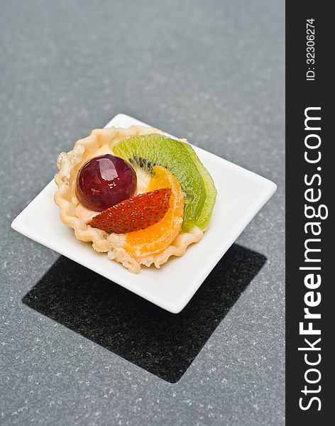 Bite size of fruit tart on small white plate on black table