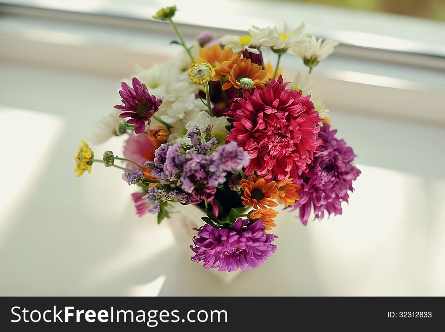 On the window sill is a bouquet of pink roses in a beautiful decorative vase. On the window sill is a bouquet of pink roses in a beautiful decorative vase