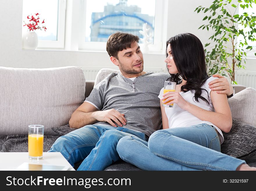 Young couple sitting on a couch and drinking orange juice. Young couple sitting on a couch and drinking orange juice