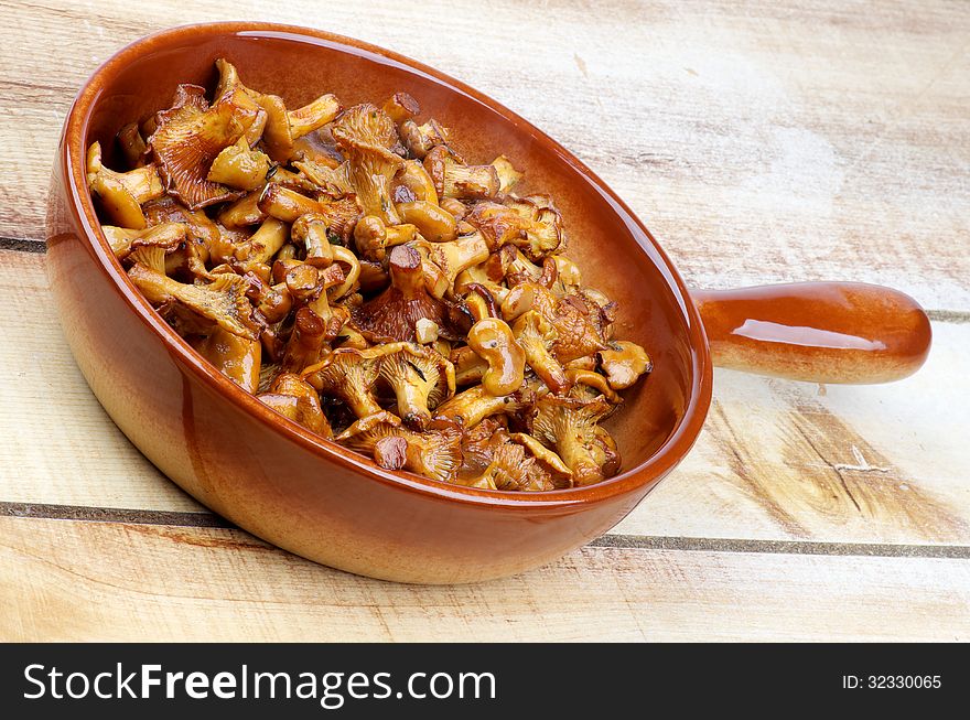 Delicious Roasted Chanterelles in Brown Frying Pan closeup on Wood background