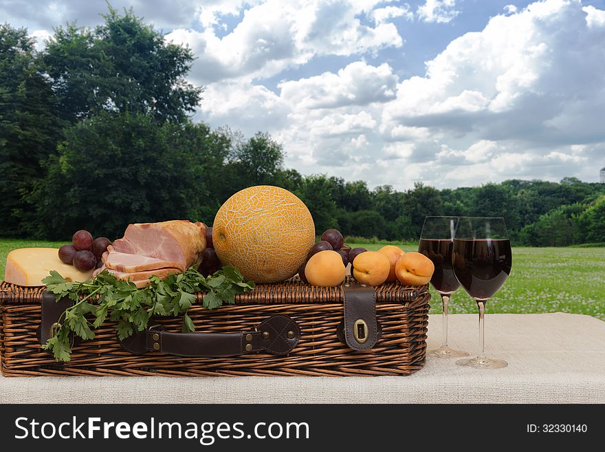 Fruit, wine, ham, cheese and basket in a forest. Fruit, wine, ham, cheese and basket in a forest