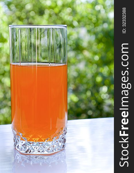 The photo shows a glass of juice in a tall glass on the background of green leaves.