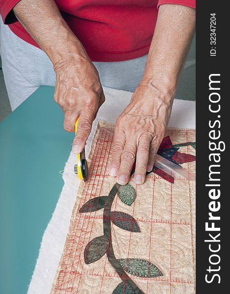 A quilter squares up the corners of a quilt using a right angle ruler and cutter. A quilter squares up the corners of a quilt using a right angle ruler and cutter.