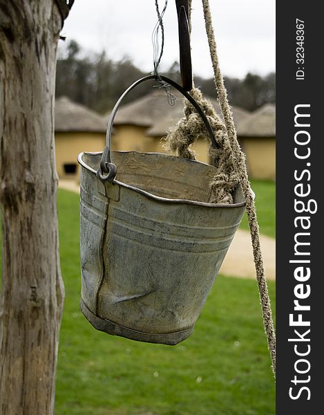 Bucket of a water well with African cabins in the background