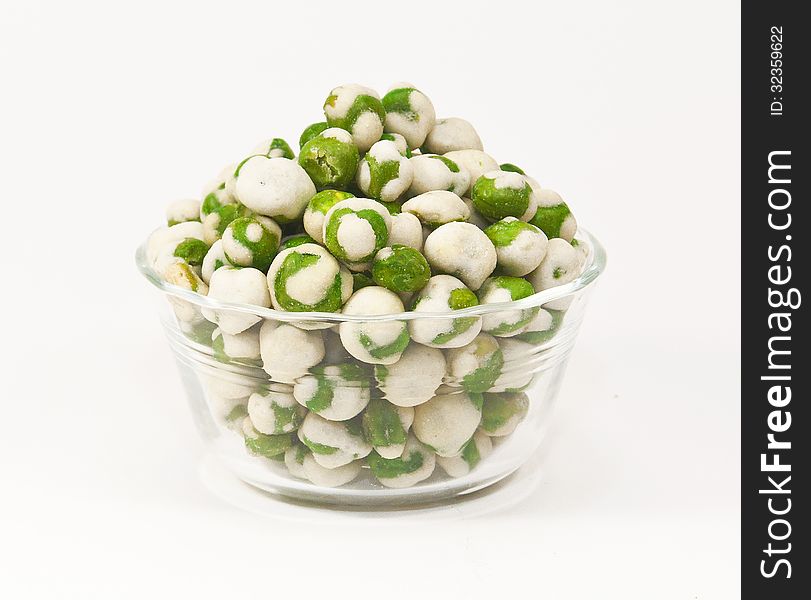 Green and white wasabi peas in a glass bowl against a white background. Green and white wasabi peas in a glass bowl against a white background