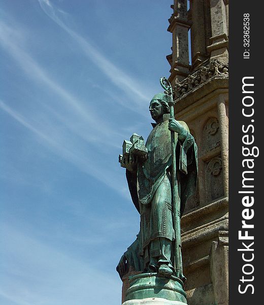 Bronze statue of bishop adorns stone memorial sculpture against blue sky with wispy clouds. Bronze statue of bishop adorns stone memorial sculpture against blue sky with wispy clouds