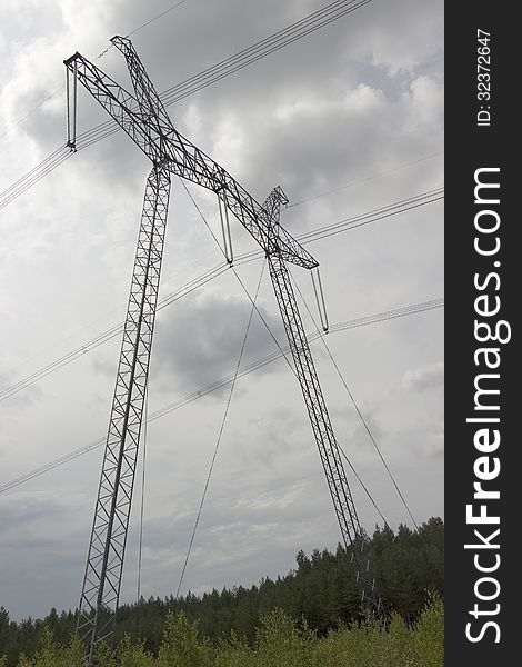 High-voltage support of the power line on the background of blue sky with clouds. High-voltage support of the power line on the background of blue sky with clouds