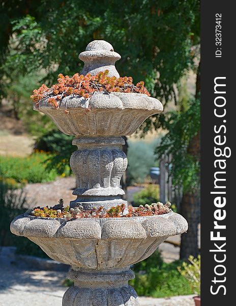 Stone water fountain with plants in on sunny day in garden