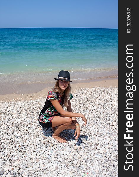Woman kneeling by the sea on a rocky beach wearing a hat. Woman kneeling by the sea on a rocky beach wearing a hat