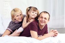 Little Girl, Father And Mother Lie On Bed And Smile Stock Photos