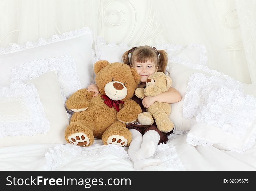 Little girl sits bed with pillows and teddy bears