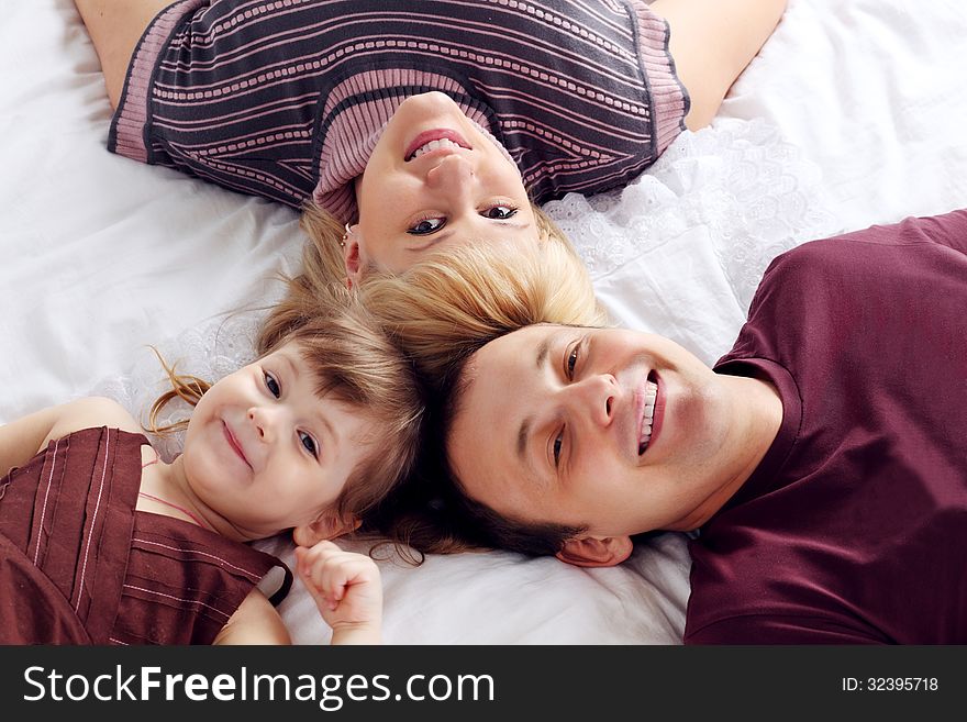 Happy Father, Little Daughter And Mother Lie On Bed