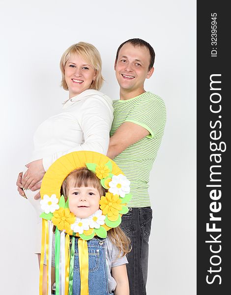 Happy pregnant wife and husband hold belly and little daughter stands near them on white background. Focus on parents. Happy pregnant wife and husband hold belly and little daughter stands near them on white background. Focus on parents.