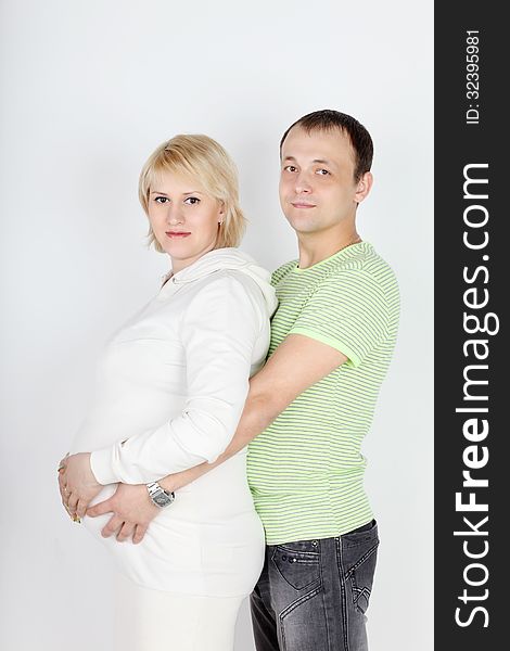 Happy pregnant wife in white and husband hold belly on white background.