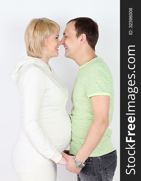 Happy pregnant wife and husband touch each other noses and laugh on white background.