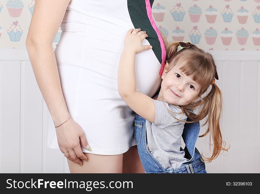 Happy little daughter touches belly of her mother