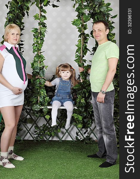 Little girl sits on swing under green ivy and father and pregnant mother swing she. Little girl sits on swing under green ivy and father and pregnant mother swing she.