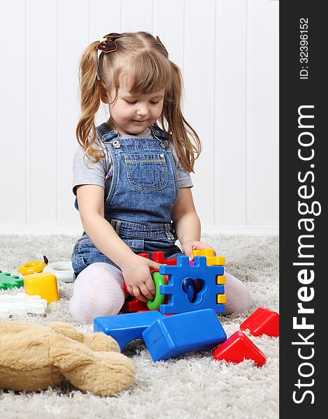 Happy little girl play colorful toys on soft carpet at home.