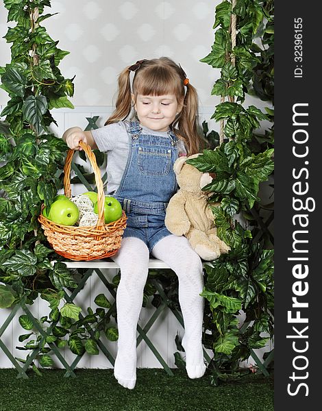 Happy little girl sits on swing under green ivy with teddy bear and basket with apples. Happy little girl sits on swing under green ivy with teddy bear and basket with apples.